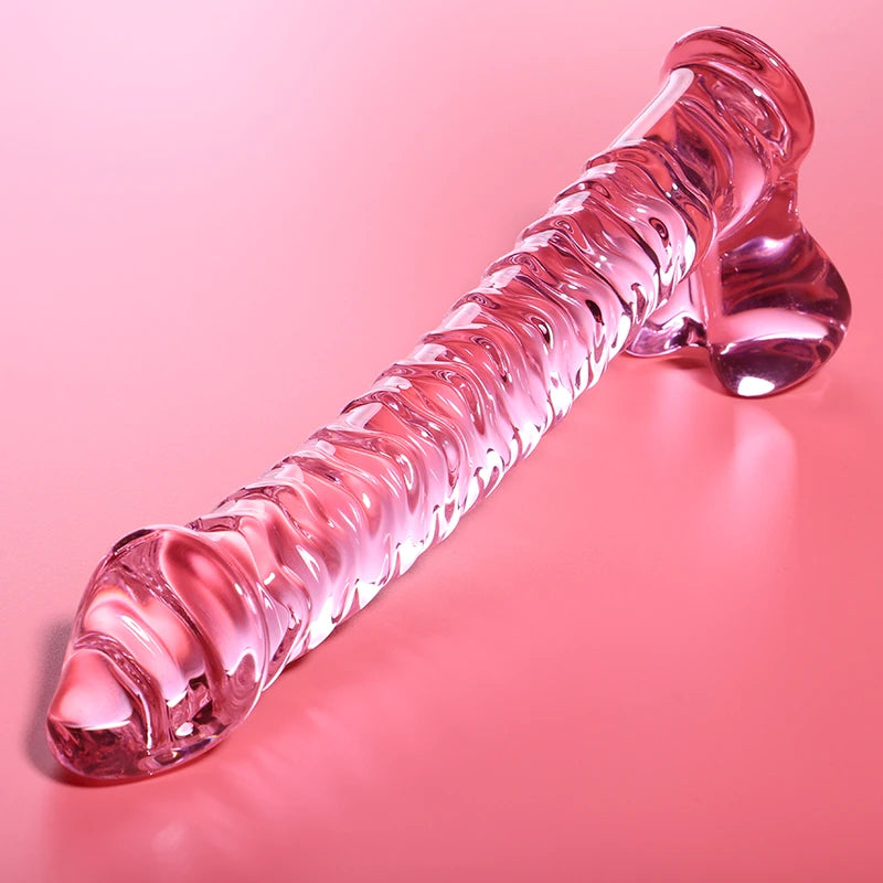 Godemichet en verre transparent rose avec forme allongée, reliefs ondulés et base élargie sur fond rose