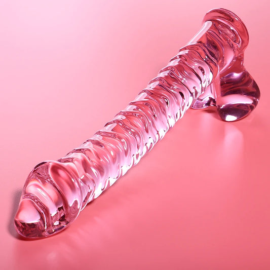 Godemichet en verre transparent rose avec forme allongée, reliefs ondulés et base élargie sur fond rose