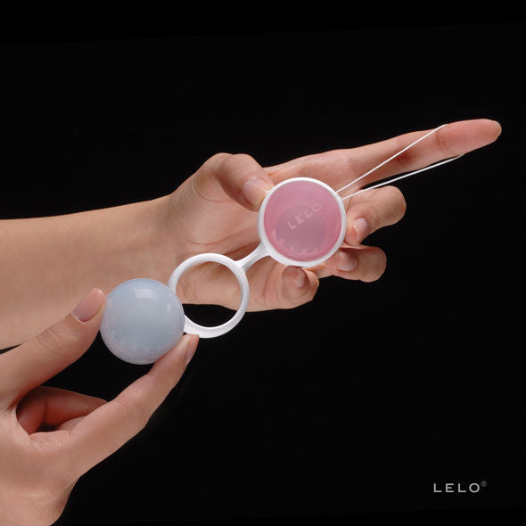 Main présentant deux boules de Geisha pastel bleu et rose avec cordon blanc