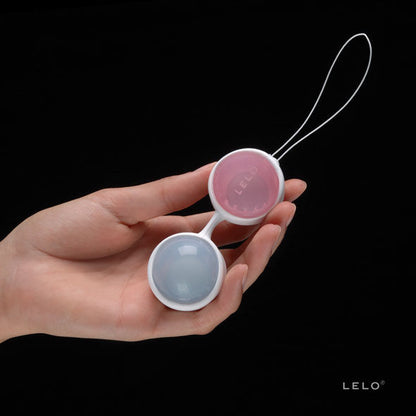 Main tenant deux boules de Geisha bleu et rose reliées par une tige blanche