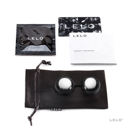 Boules argentées avec cordon noir, pochette noire et documentation posées sur fond clair